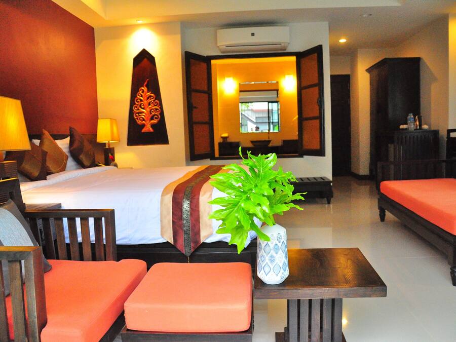 Una habitación de hotel con una cama, dos sillas naranjas, una mesa de madera y una planta en maceta.