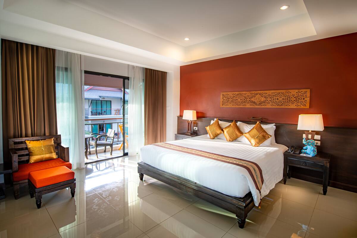 A hotel room with a large bed, two bedside tables with lamps, a sofa with cushions, and a view of the outside balcony.