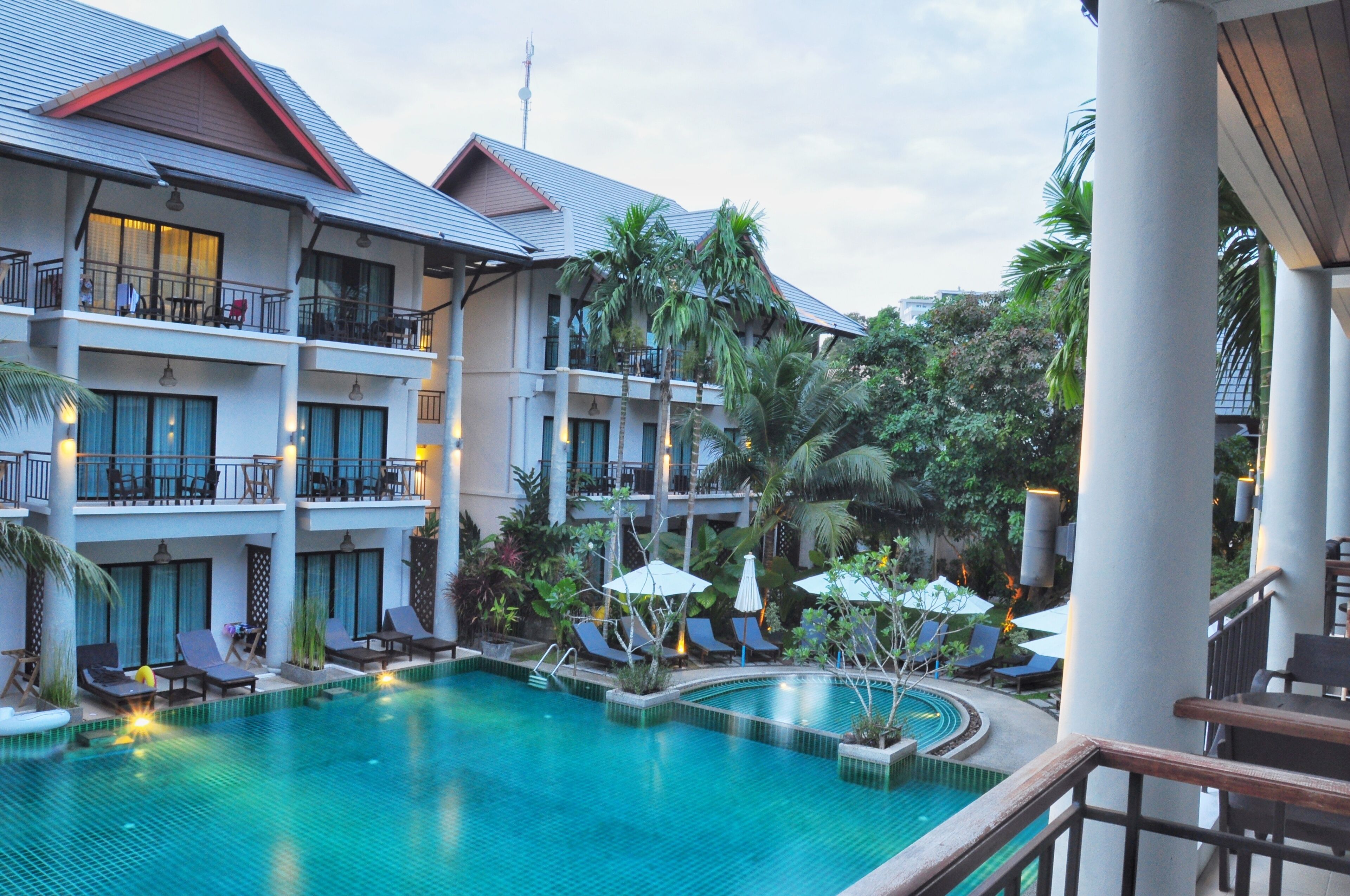 A hotel with a swimming pool, multiple balconies, and lush greenery.