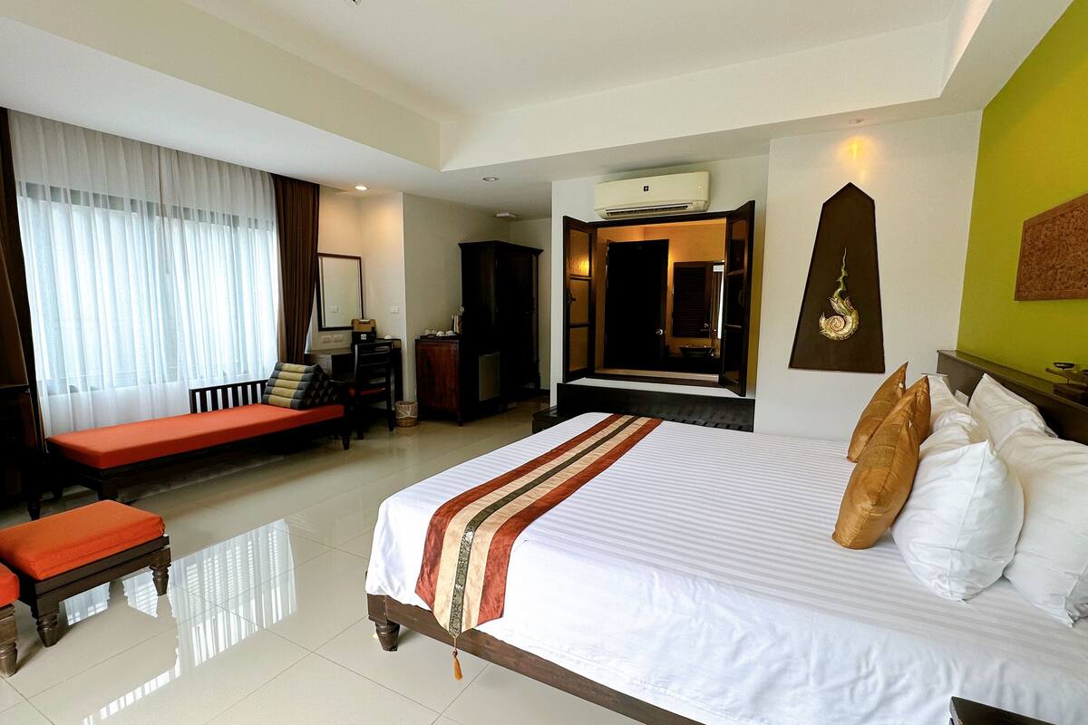 A hotel room with a large bed, a bench, a desk, a wardrobe, and a mirror.