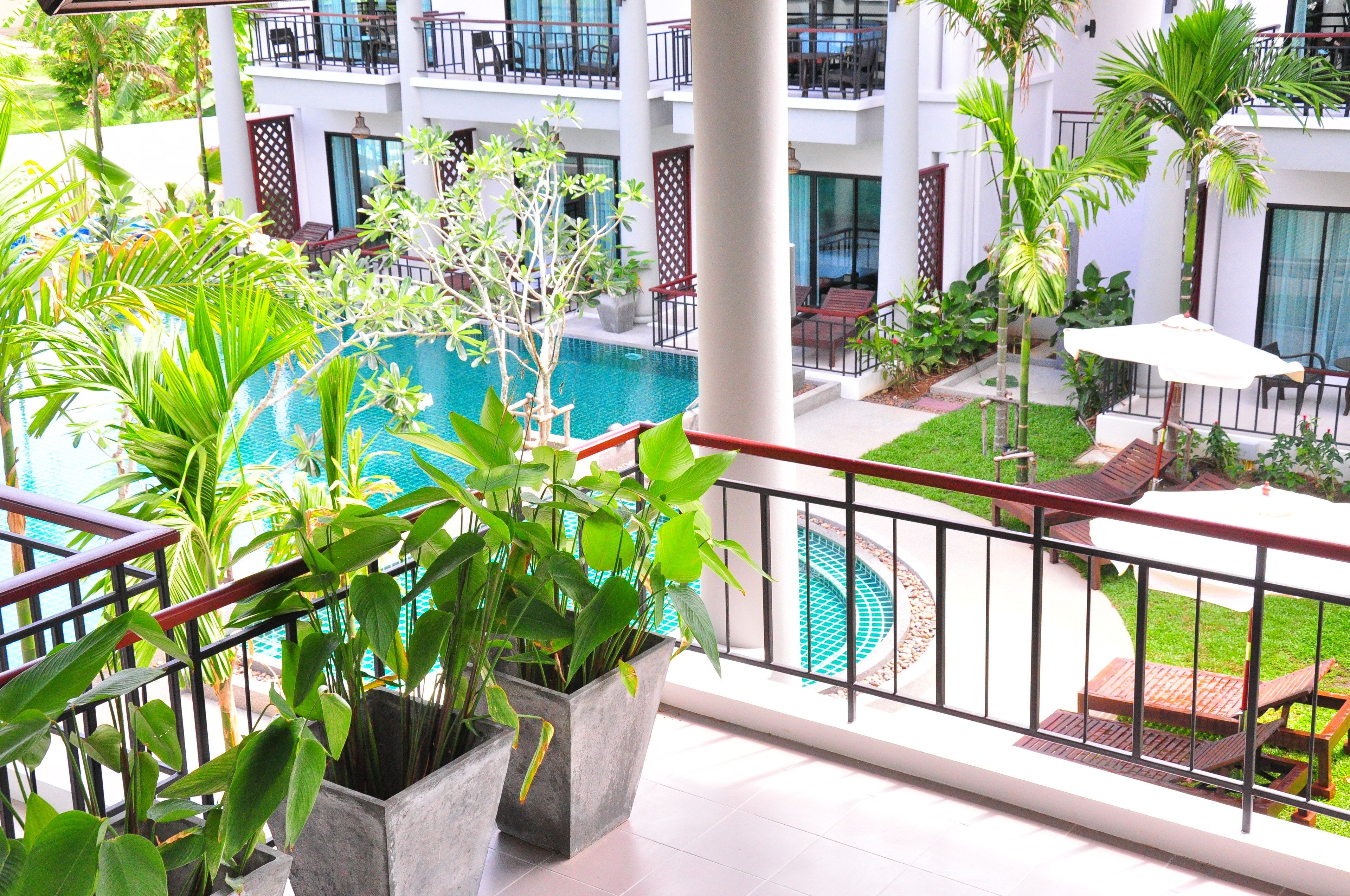 A hotel balcony with a pool, potted plants, outdoor furniture, and a view of the pool area.