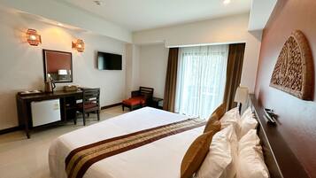 Una habitación de hotel con una cama grande, un escritorio con una silla, un televisor y una ventana con cortinas.