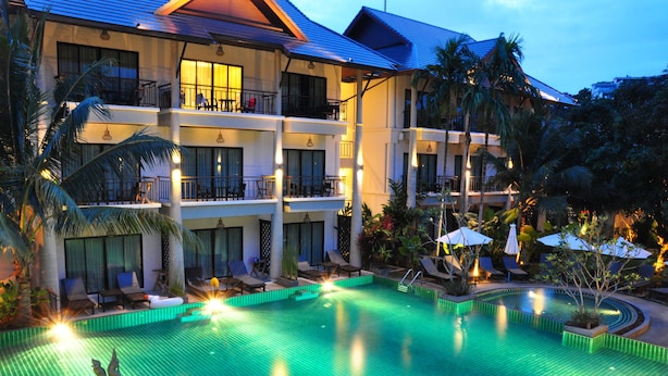 Un hotel con una grande piscina esterna, numerosi balconi e una rigogliosa vegetazione tropicale.