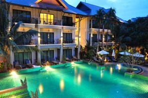Un hotel con una amplia piscina exterior, varios balcones y exuberante jardinería tropical.