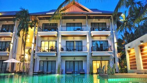 Un hotel a più piani con balconi, piscina e palme.