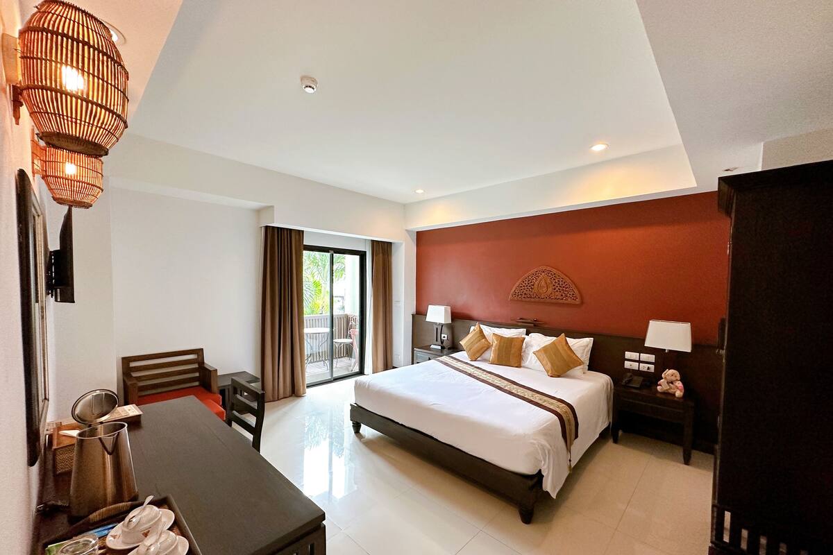 A hotel room with a large bed, bedside tables, a desk with a chair, a sliding glass door to an outdoor area, and a decorative wall piece.