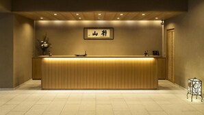 A reception desk with a wooden finish, a framed sign above it, and a vase with flowers to the left. - Seizansou (Uji)