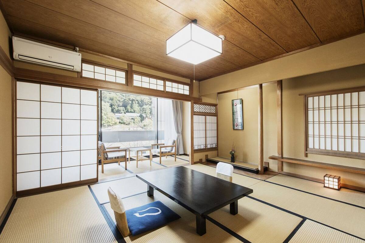 Um quarto japonês tradicional com tatames, uma mesa baixa, portas deslizantes e vista para o exterior.