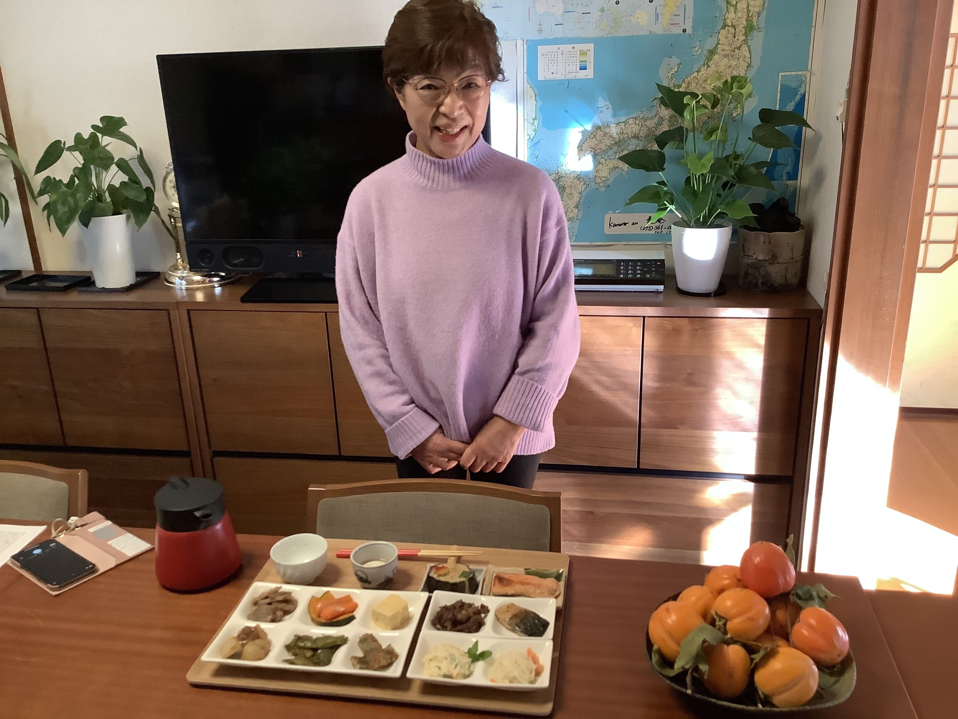 A person standing in a room with a dining table set with various dishes, a TV, and a map on the wall.