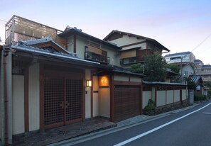 A traditional Japanese house with a wooden gate, a lit sign, and a tiled roof. - Kamuro An (Kyoto)