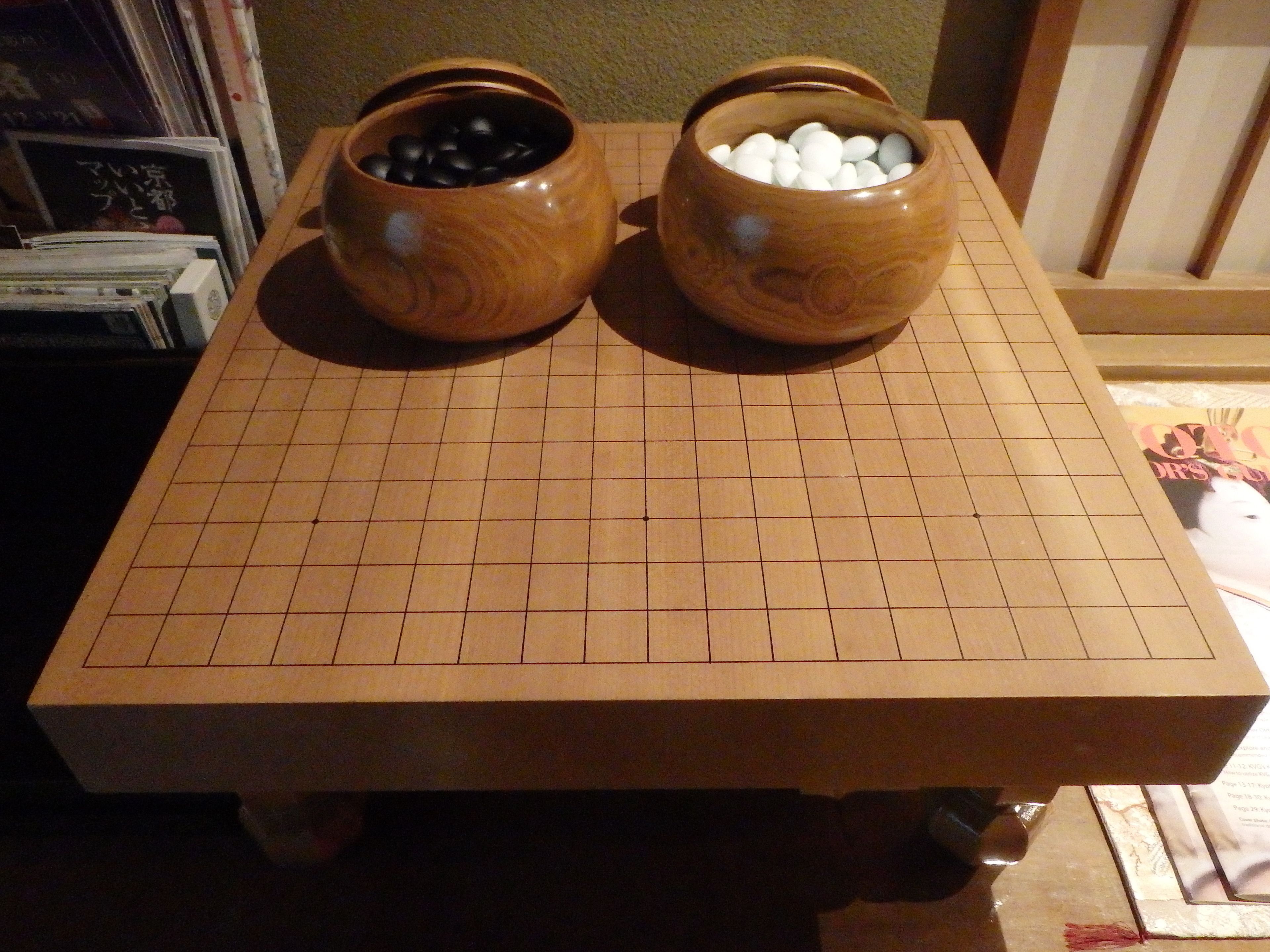 Een houten tafel met een ruitpatroon, twee houten kommen met zwart-wit objecten, en een betegelde vloer.