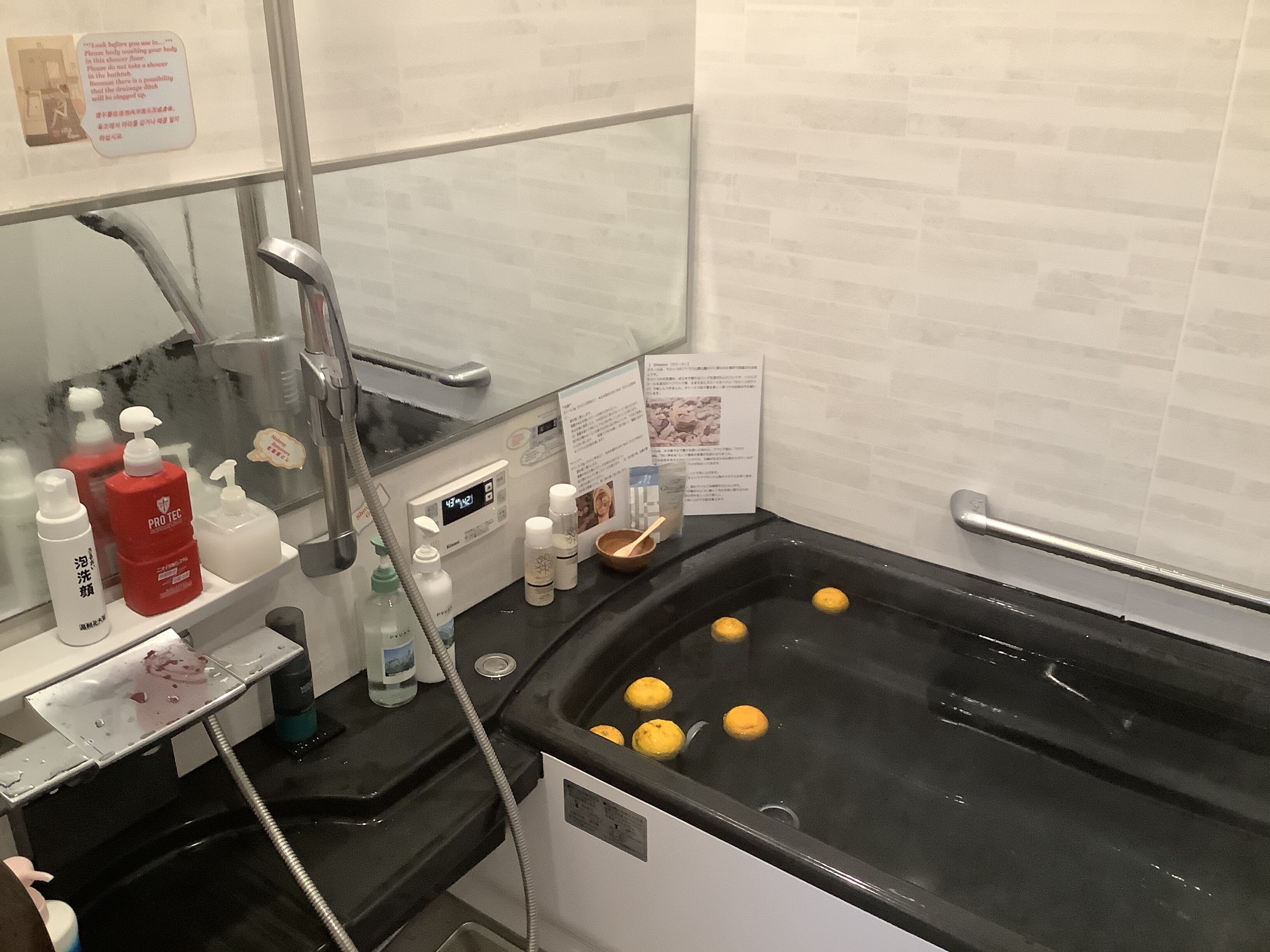 Un baño con una bañera negra, una ducha de mano y varios artículos de aseo en un mueble.