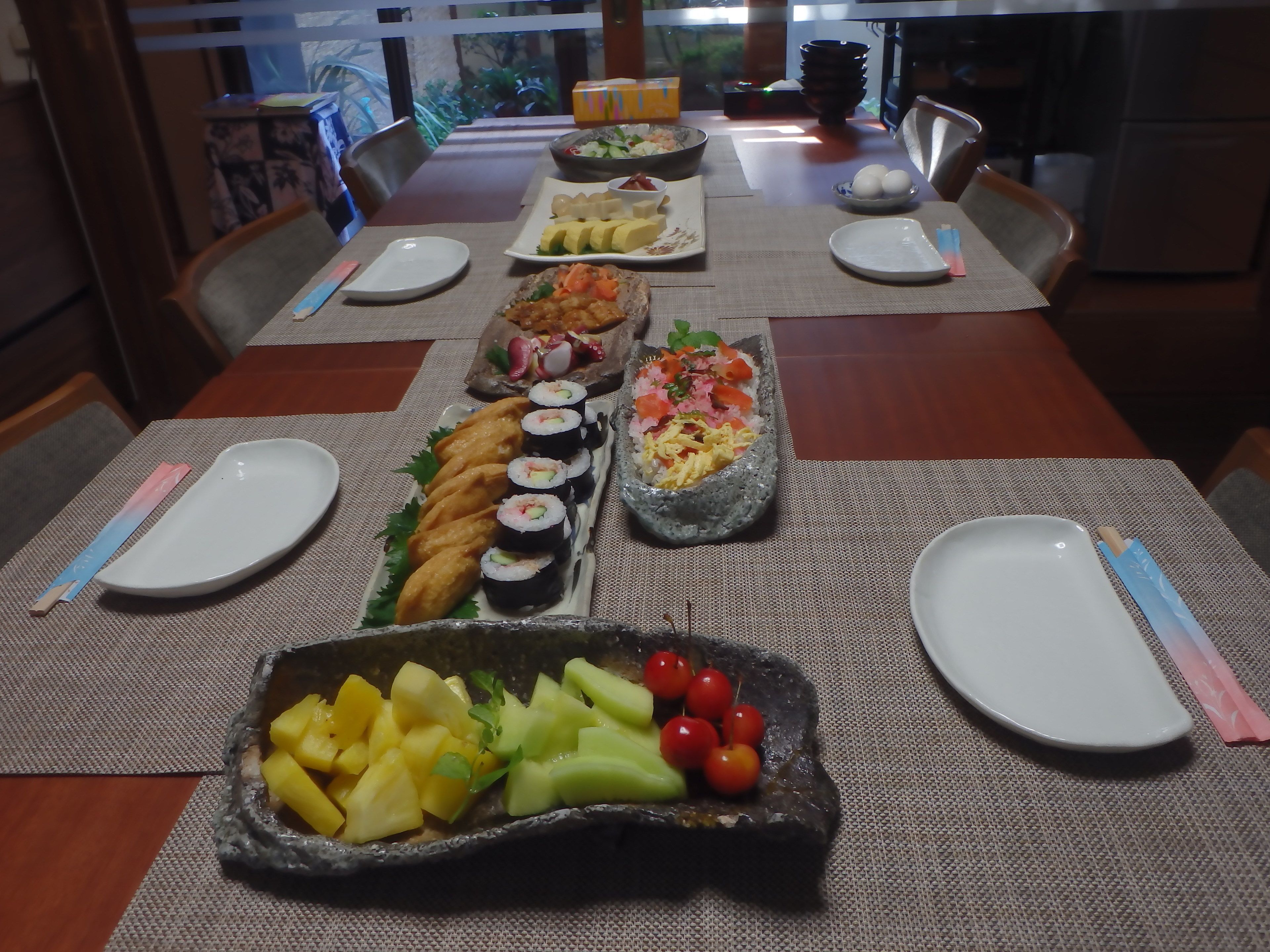 A dining table set with various dishes, including sushi, sashimi, and a fruit platter.