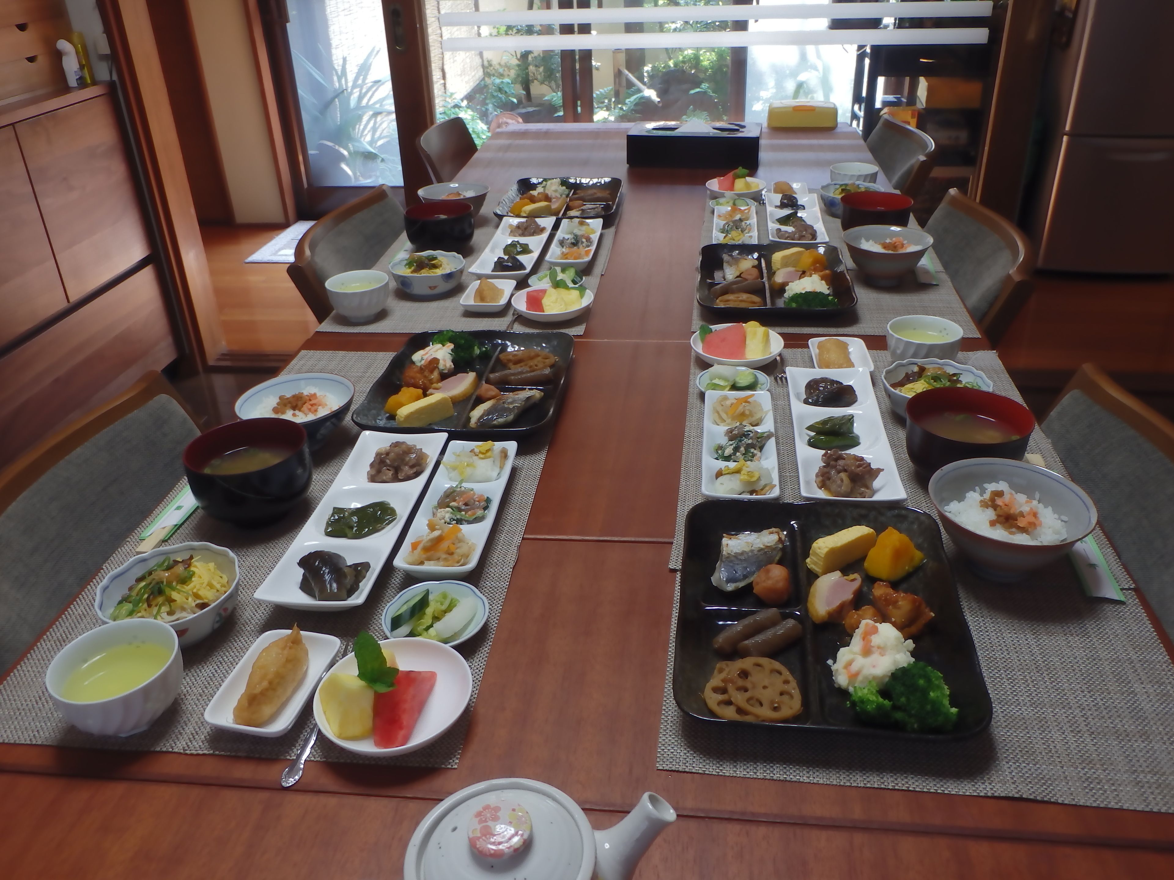 Una comida tradicional japonesa dispuesta con diversos platos y cuencos sobre una mesa, rodeada de sillas.