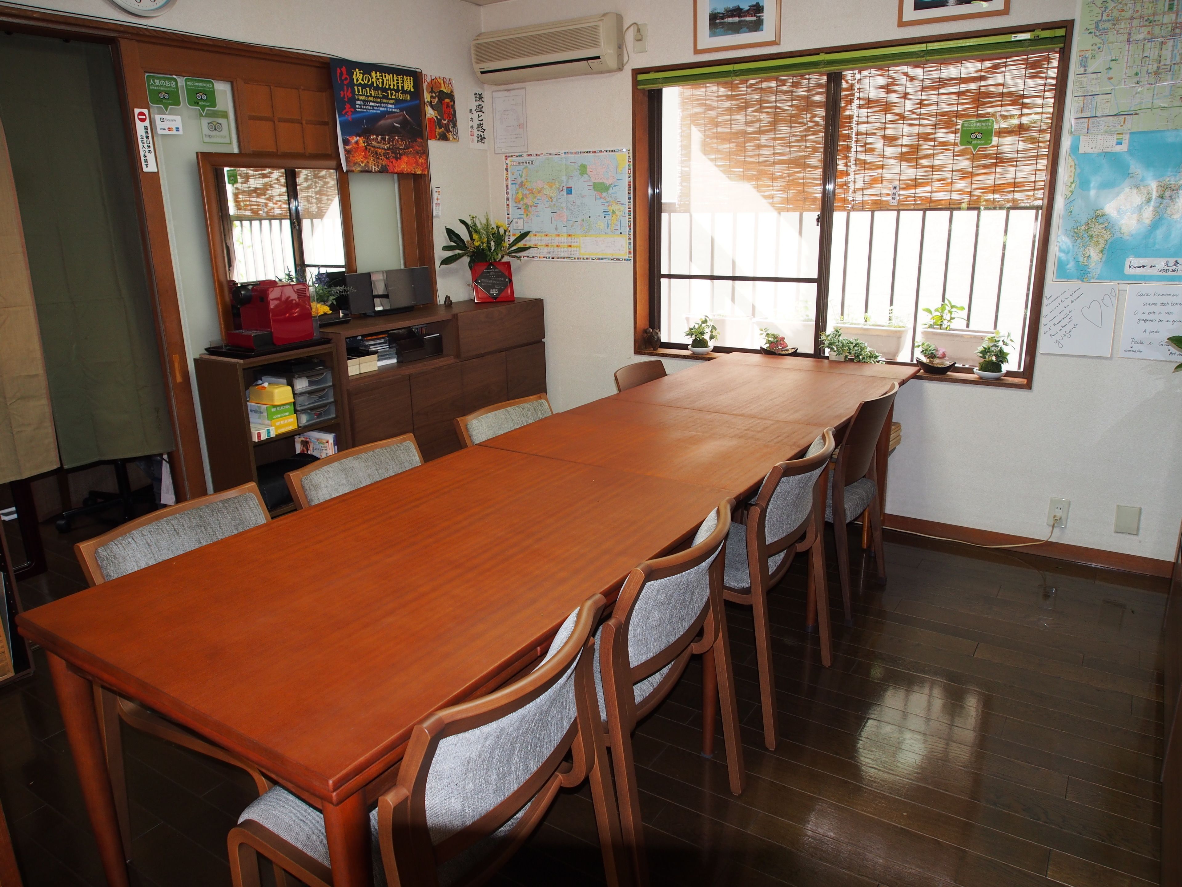 A conference room with a long wooden table and chairs, a bookshelf, a map on the wall, and a window with blinds.