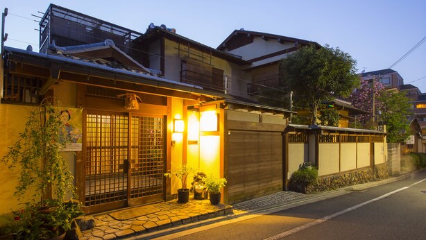 A traditional Japanese building with a wooden gate, potted plants, and a stone-paved entrance. - Kamuro An (Kyoto)