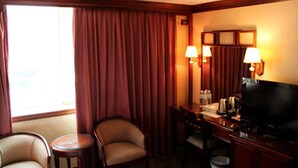 A hotel room with a large window, a desk with a television, two chairs, and lamps on the wall. - Meadow Hotel (Taipei)