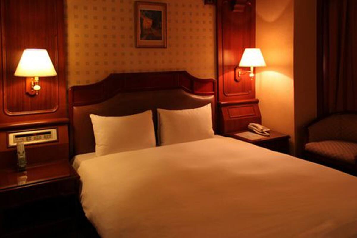A hotel room with a large bed, two bedside lamps, a nightstand with a phone, and a wall-mounted picture.