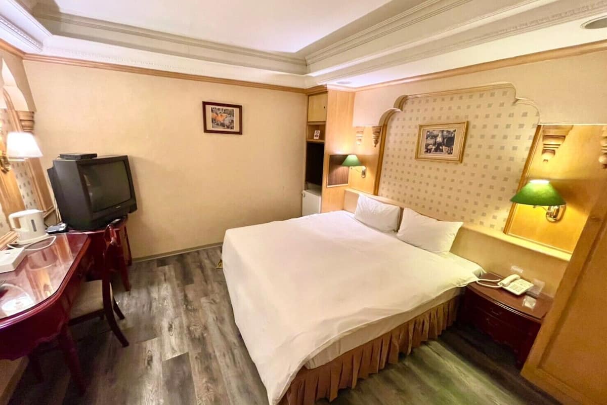 A hotel room with a bed, a desk, a television, a telephone, and two wall-mounted lamps.