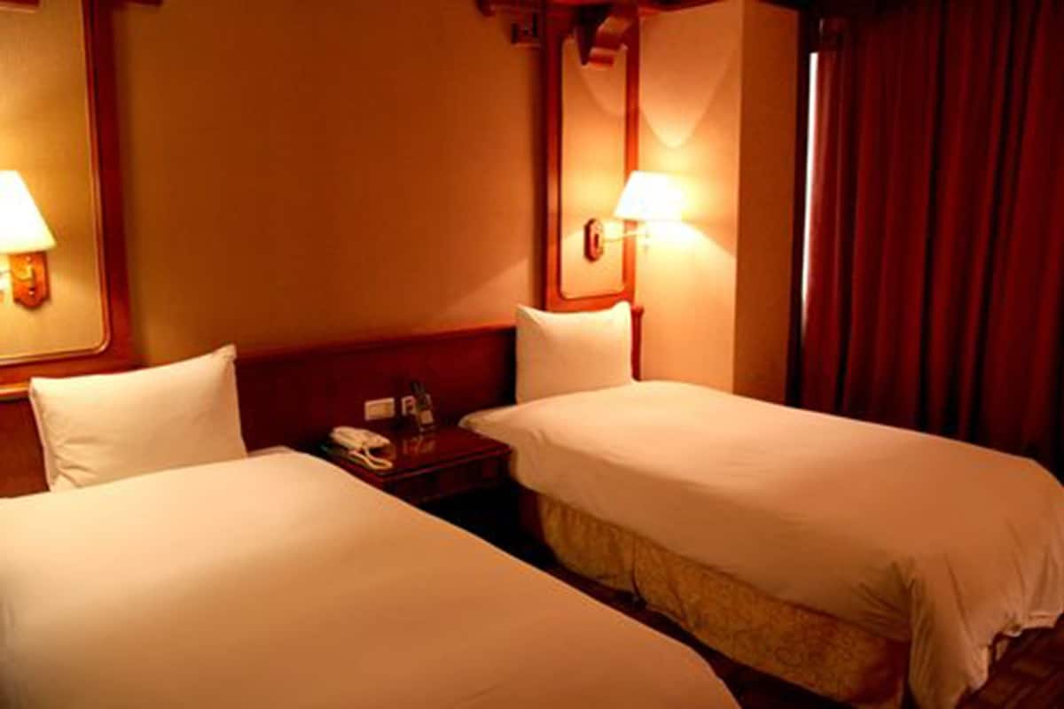 A hotel room with two single beds, a nightstand with a lamp, and a mirror on the wall.