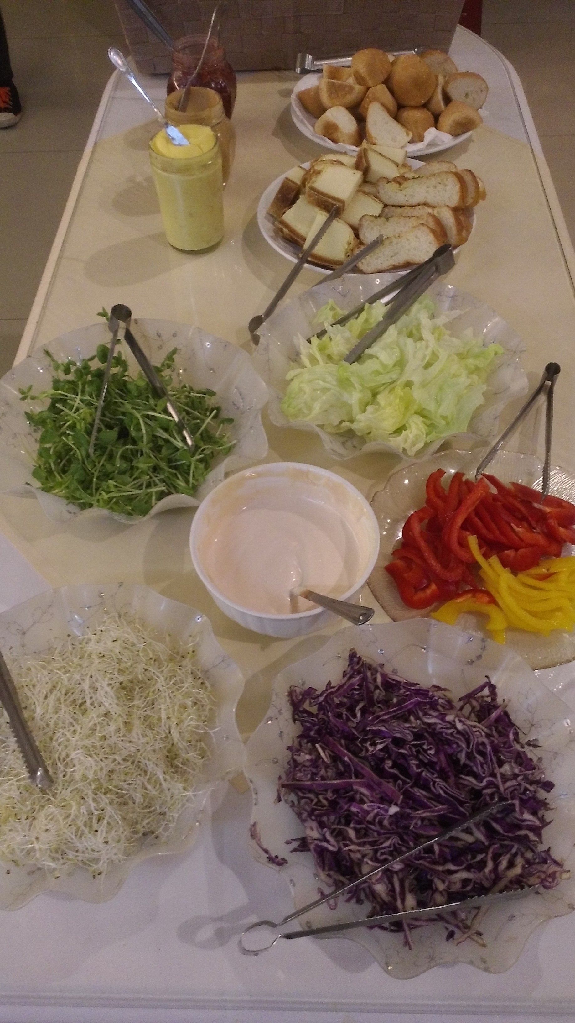A buffet table with various food items including salads, bread, and a dipping sauce.