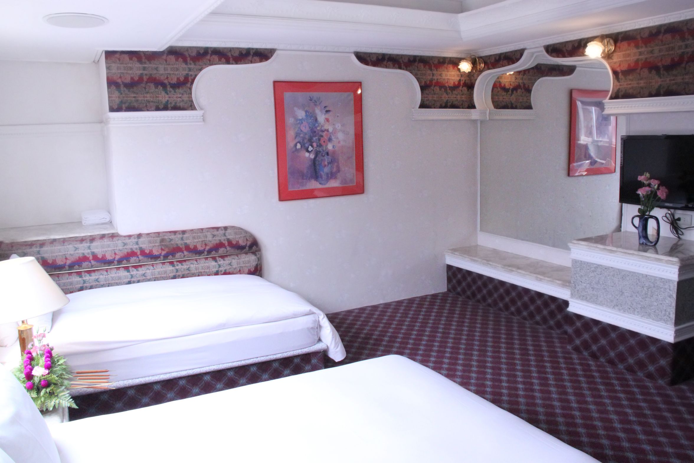 Ein Hotelzimmer mit einem Bett, einem Nachttisch mit Lampe, einem Spiegel und einem gerahmten Kunstwerk an der Wand.