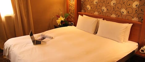 Habitación de hotel con una cama bien hecha, una mesita de noche con una lámpara y un estampado floral en la pared.