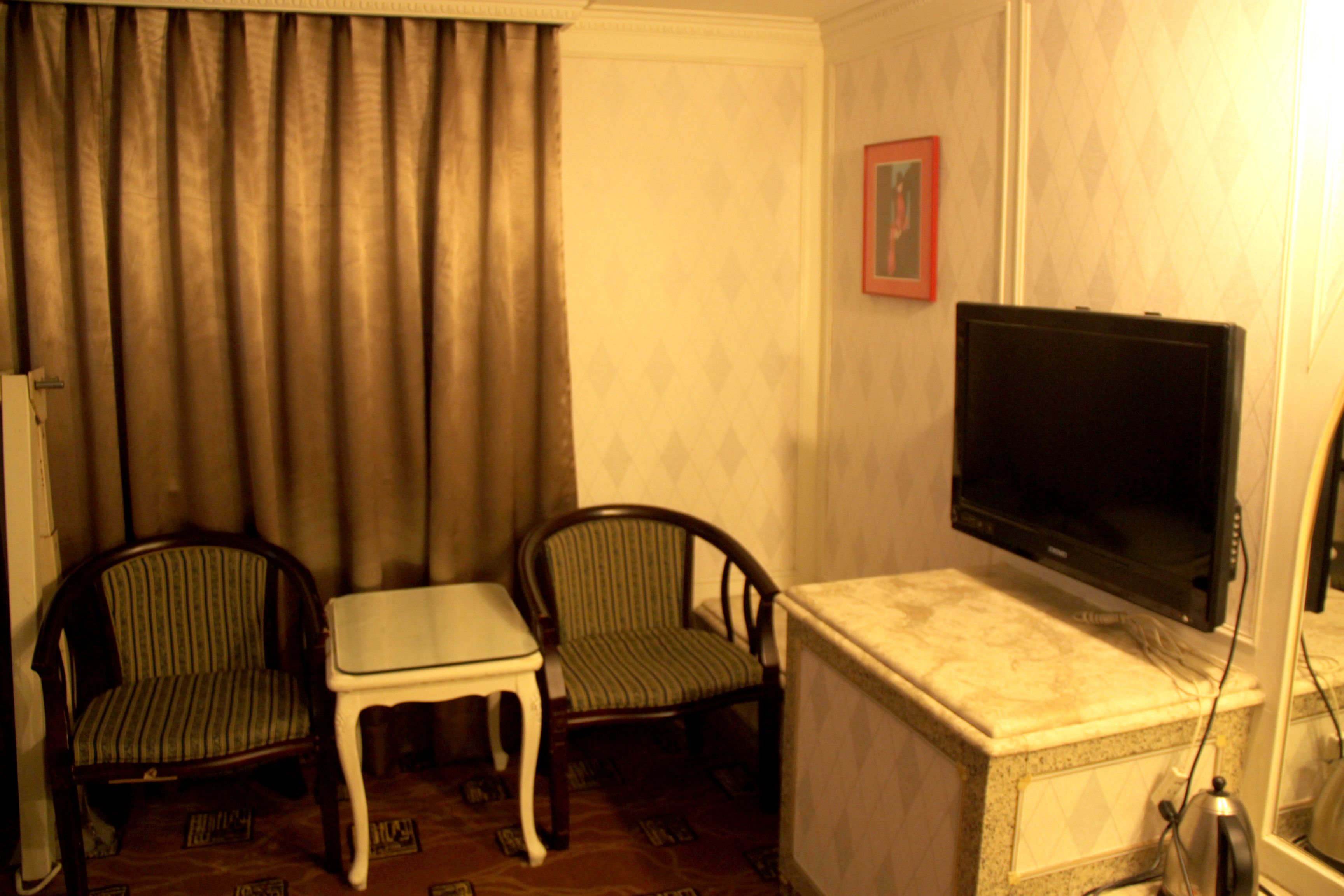 A room with two armchairs, a small table, a television mounted on a marble cabinet, and a framed picture on the wall.