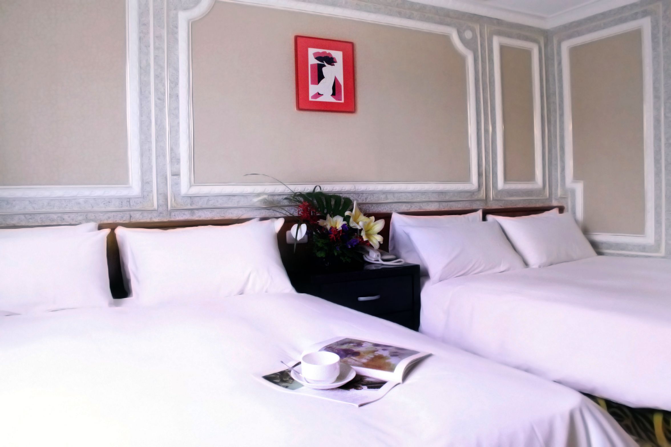 A hotel room with two beds, a nightstand with a vase of flowers, and a framed picture on the wall.