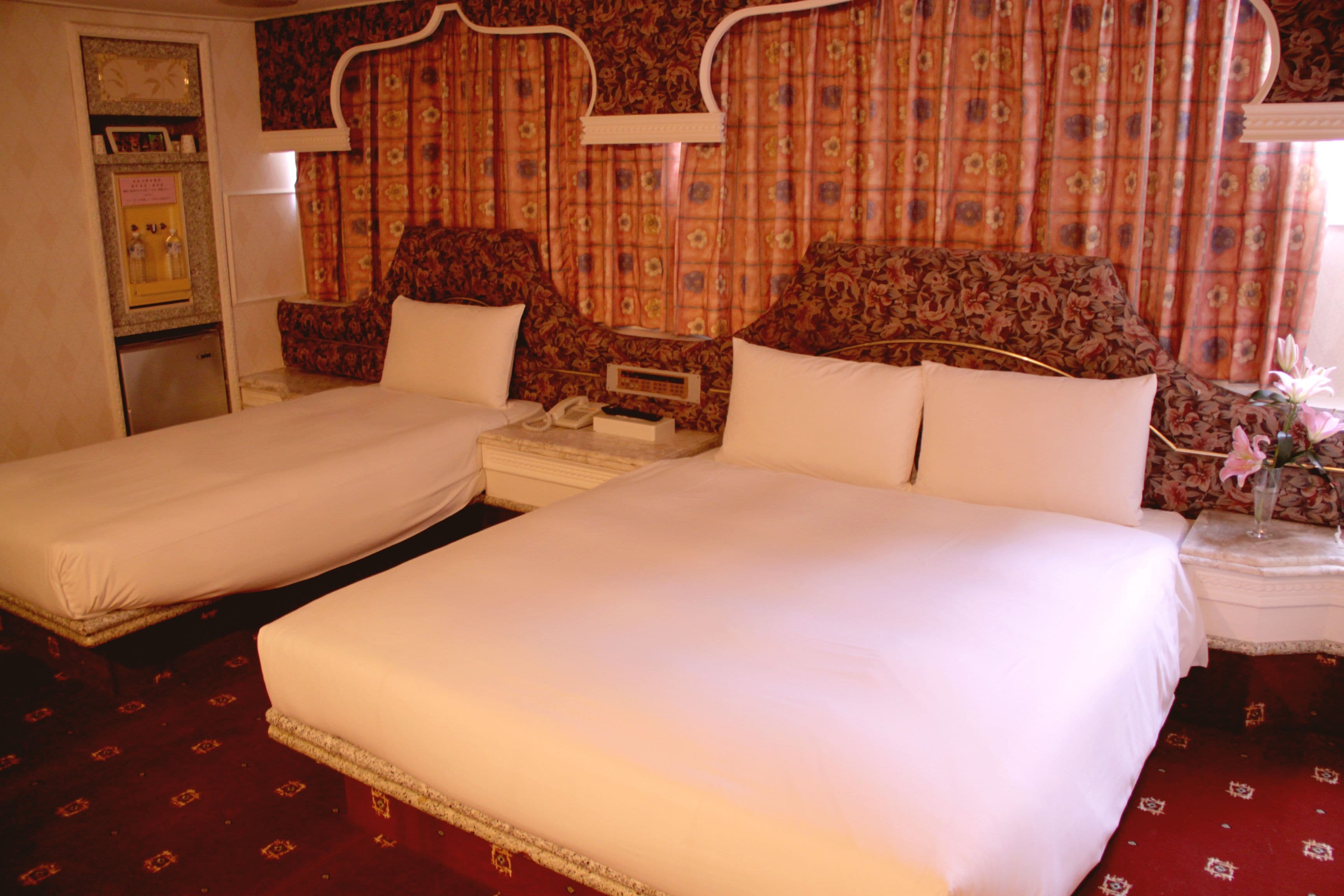 Een hotelkamer met twee enkele bedden, een klein nachtkastje met een lamp, een nachtkastje en een bloemstuk.
