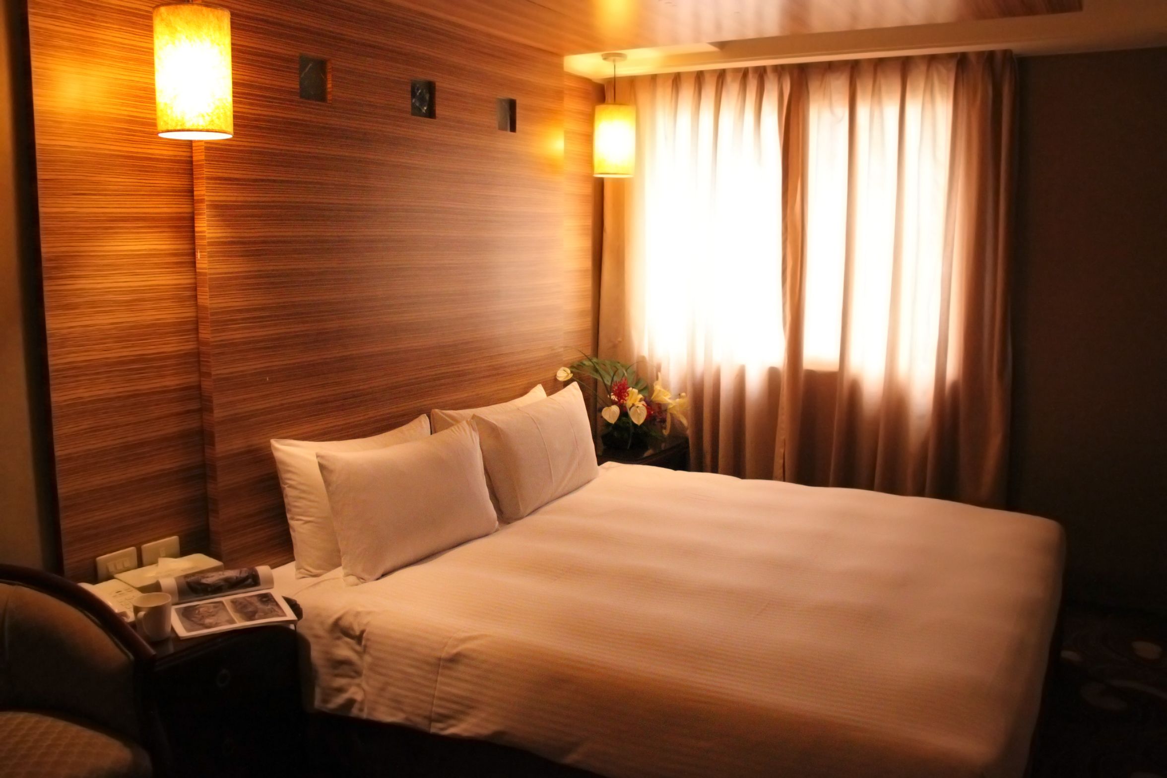 A hotel room with a large bed, a nightstand with a lamp, a chair, and a window with curtains.