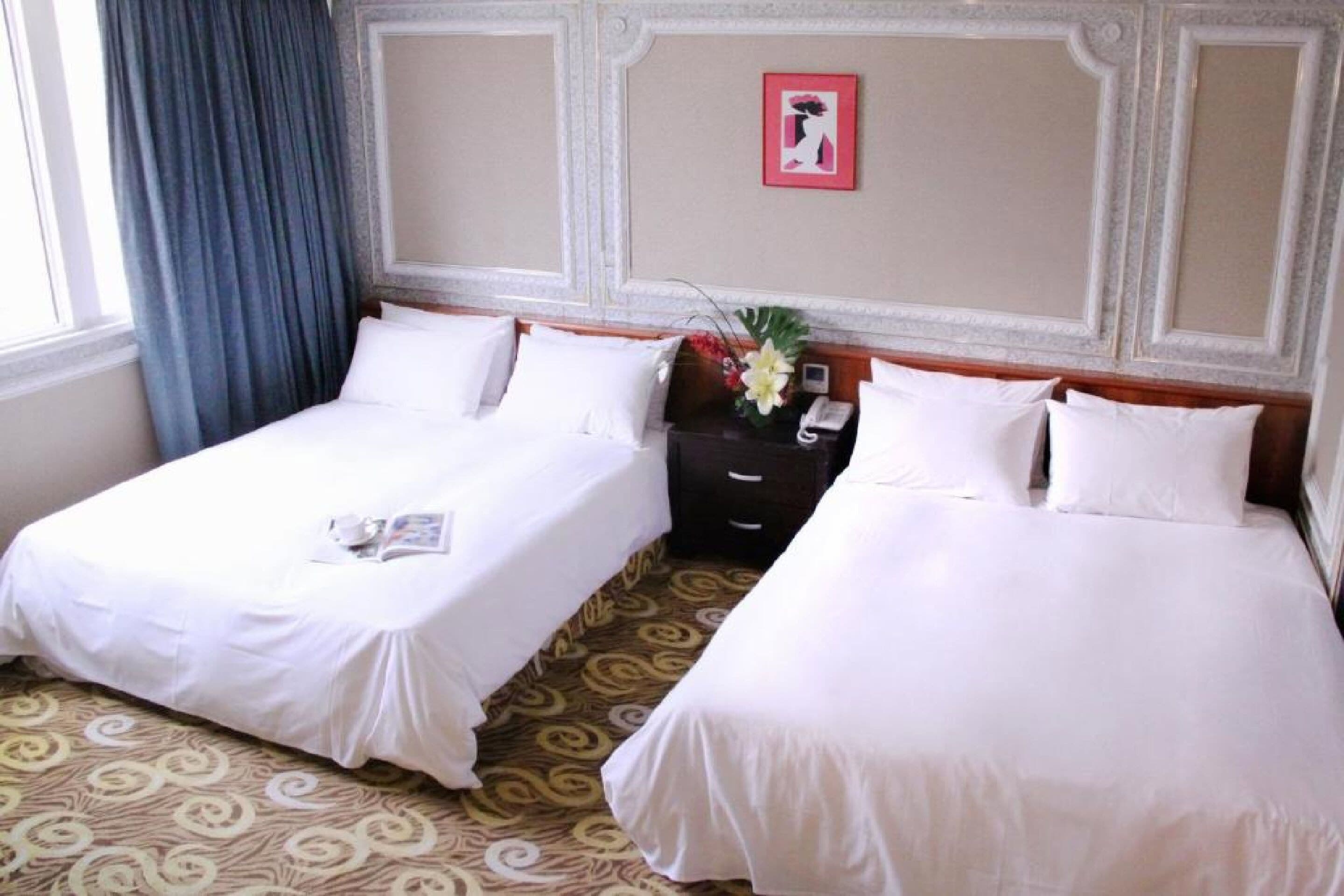 Een hotelkamer met twee eenpersoonsbedden, een nachtkastje met een telefoon en een bloevas, en een kamerbreed tapijt met dessin.