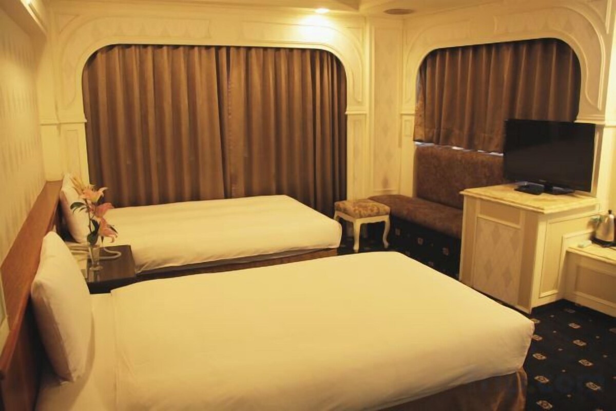 A hotel room with two beds, a television, a small table, and a window with curtains.