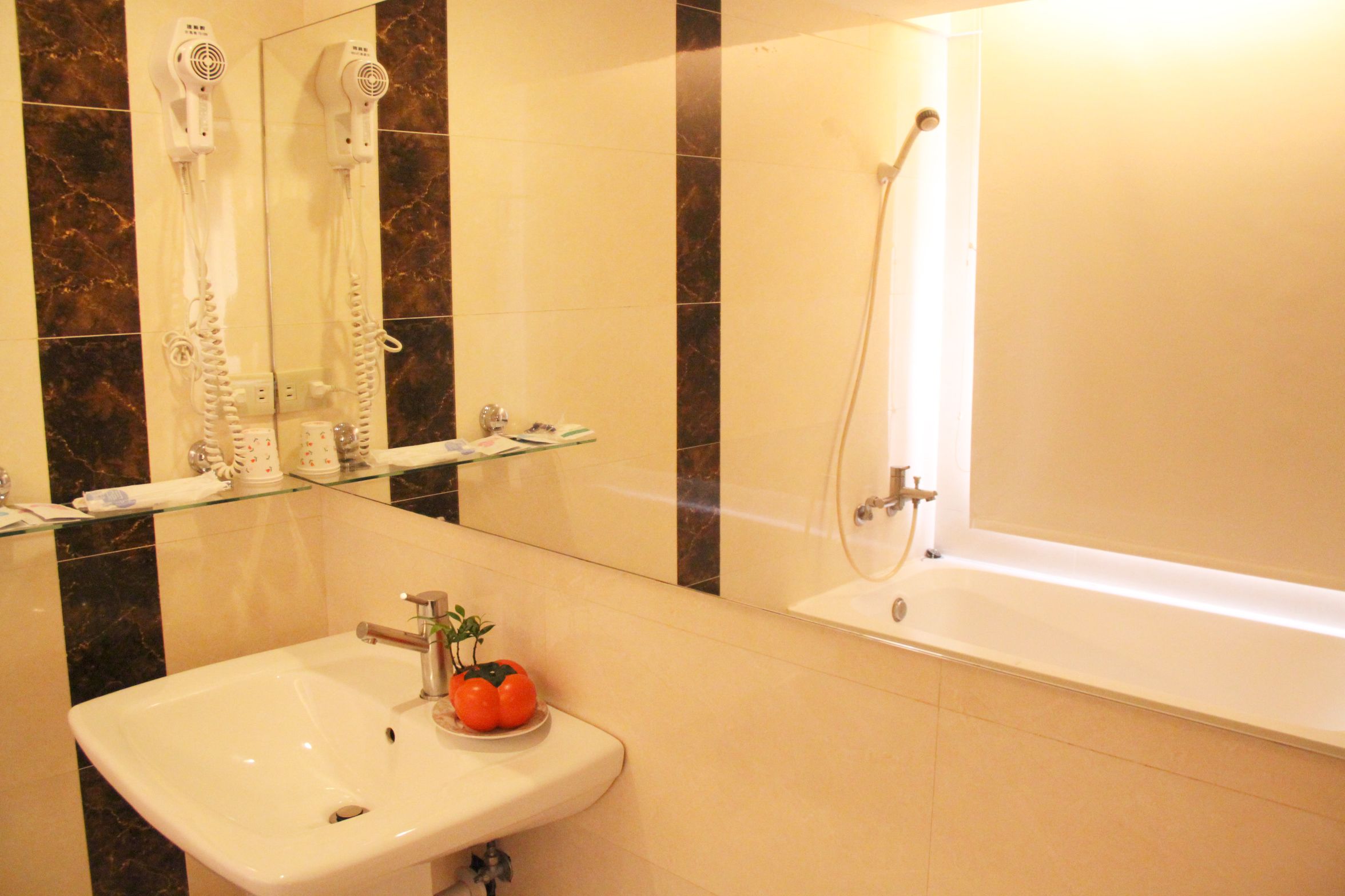 A bathroom with a white sink, a glass shelf, a mirror, a hairdryer, and a bathtub.