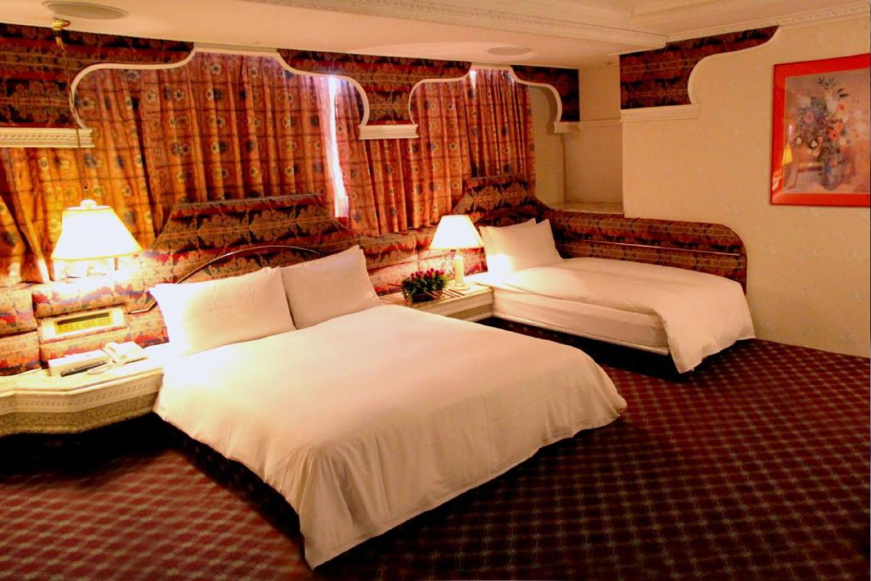 A hotel room with two beds, a patterned carpet, and a decorative headboard.