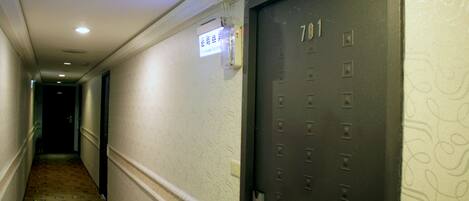Um corredor com parede estampada, uma porta com a inscrição "701" e um interruptor de luz na parede.