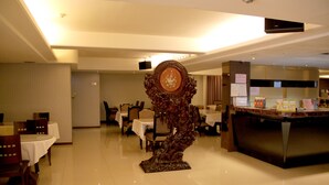 Um saguão de hotel com área de refeições, balcão de recepção e uma escultura decorativa.