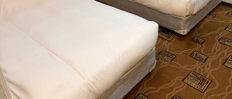 A hotel room with two single beds, a nightstand, a lamp, and a patterned carpet.