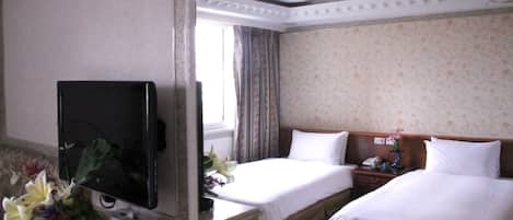 Ein Hotelzimmer mit zwei Betten, einem Fernseher, einem Schreibtisch mit Telefon und einem fenster mit Vorhängen.