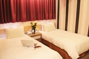 A hotel room with two beds, a nightstand with a lamp and a vase of flowers, and a laptop on one bed. - Crystal Hotel (Taipei)