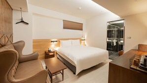 A modern hotel room with a large bed, a sofa, a desk, and a bathroom with a glass shower. - inns hotel (Kaohsiung)
