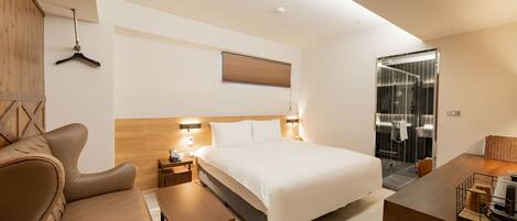 A modern hotel room with a large bed, a sofa, a desk, and a bathroom with a glass shower.