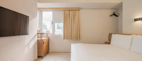 A modern hotel room with a large bed, a TV mounted on the wall, a wooden cabinet, and a window with curtains.