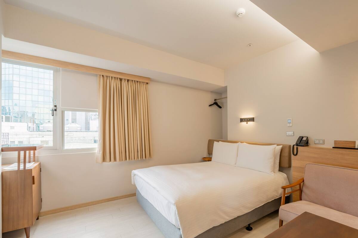 A hotel room with a bed, bedside table, chair, and a desk.