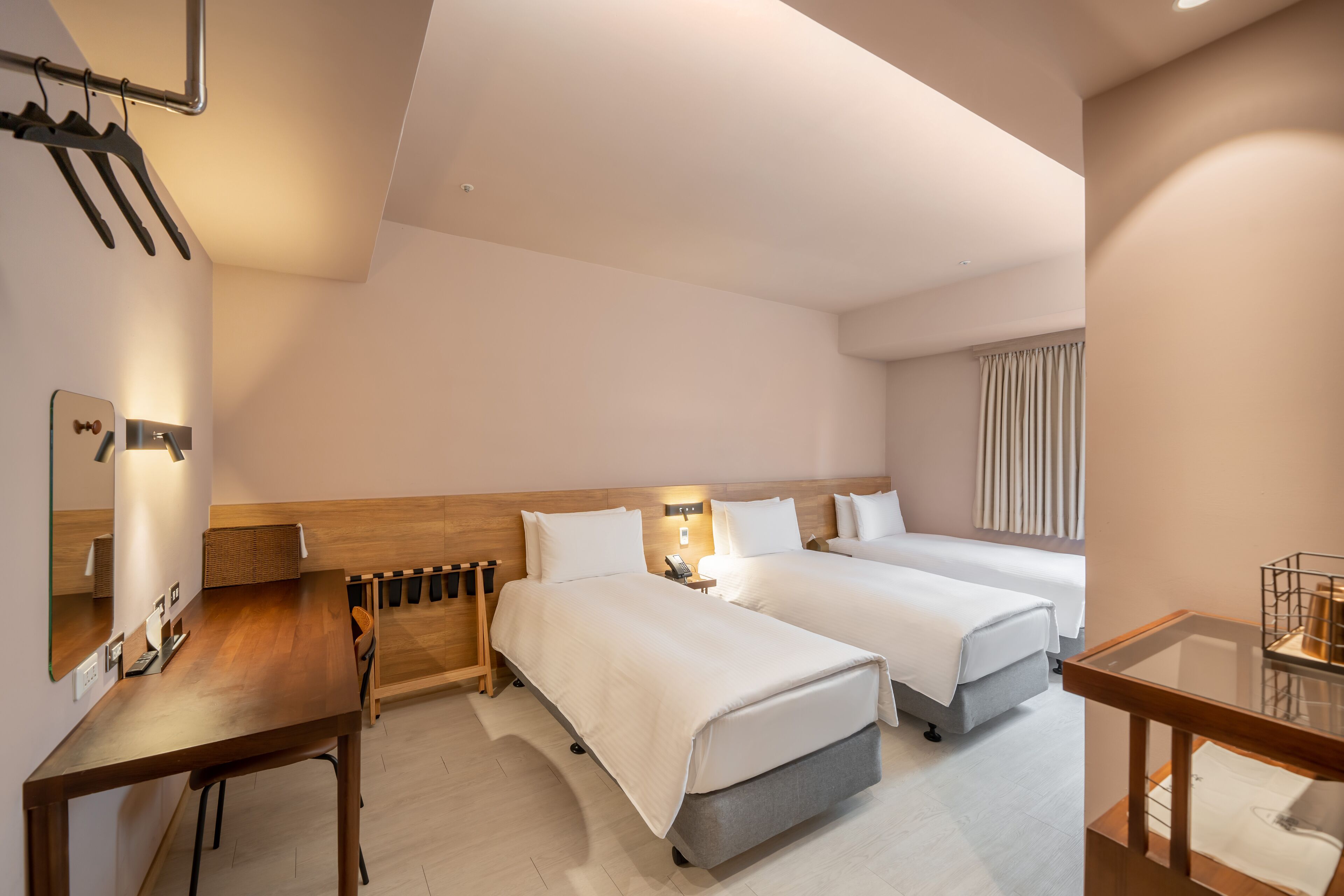 Ein modernes Hotelzimmer mit zwei Betten, einem Holztisch, einem Stuhl und einem kleinen Tisch.
