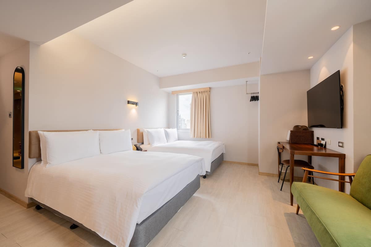 A hotel room with two beds, a desk, a television, and a green sofa.