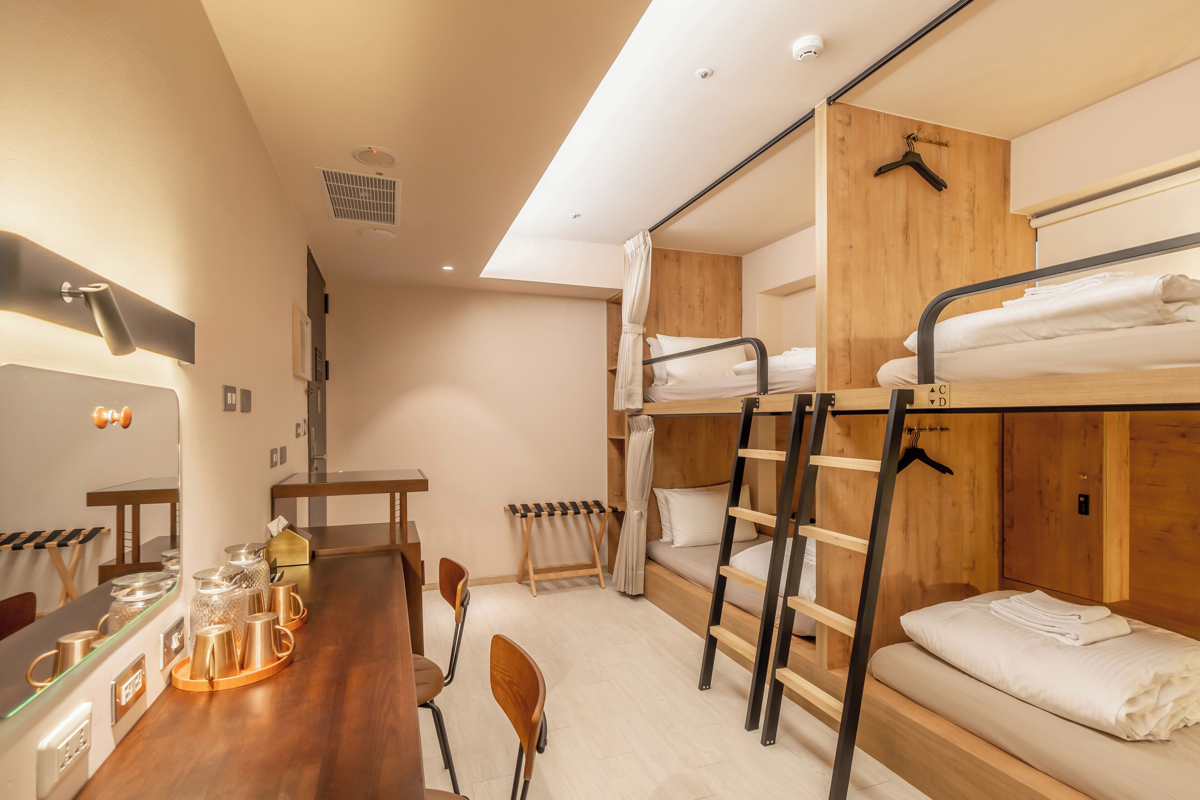 A bunk bed room with a wooden desk, chairs, and a small table with cups and a kettle.