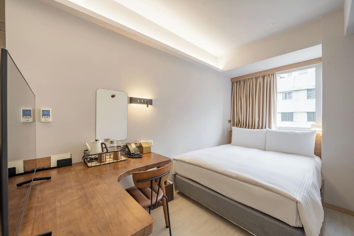 A hotel room with a bed, a desk with a chair, a telephone, and a mirror.