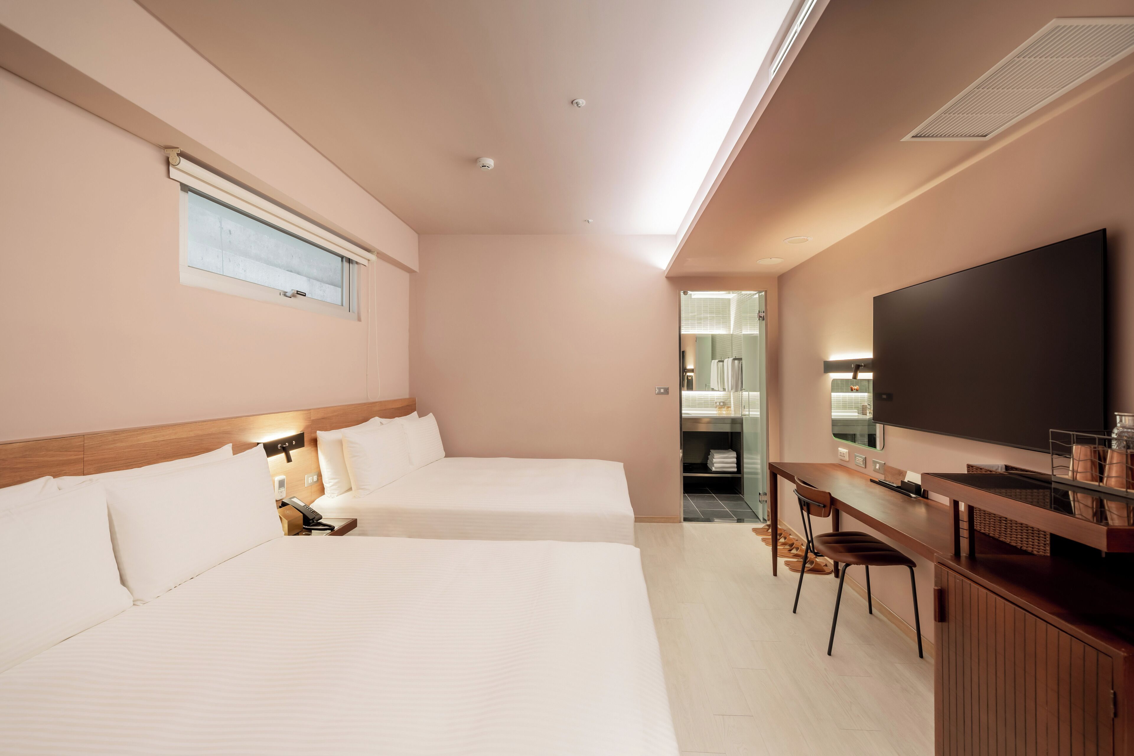 A hotel room with two beds, a desk, and a large TV.