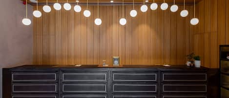 A reception desk with a wooden panel backdrop, multiple drawers, and a hanging light fixture.